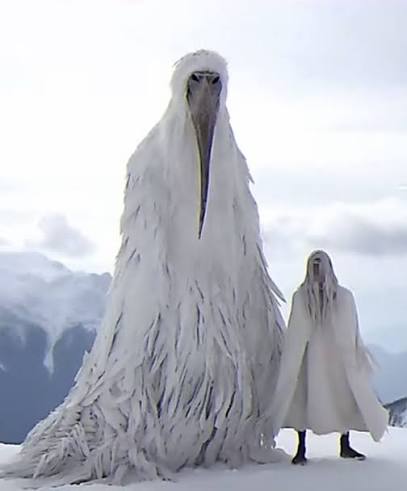 Erosion Bird — a towering white feathered guardian standing on snow beside a cloaked figure